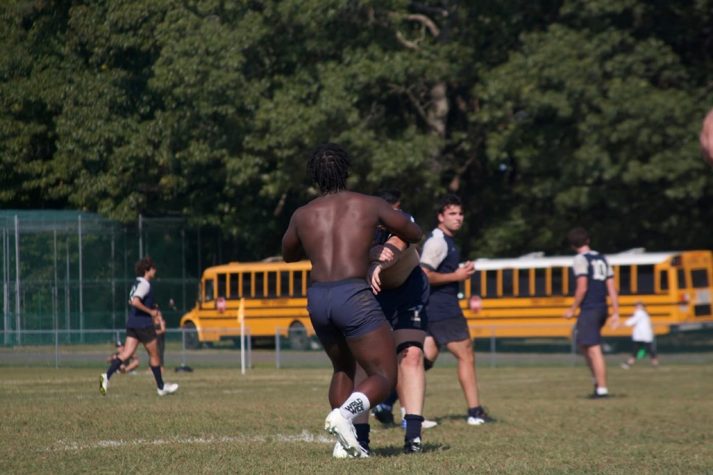 Rugby match in motion — carrying the ball past a yellow school bus